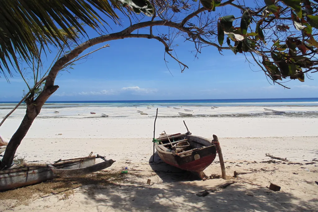 Holzboot am Strand von Kizimkazi unter einem Baum, dahinter heller Sand und Meer