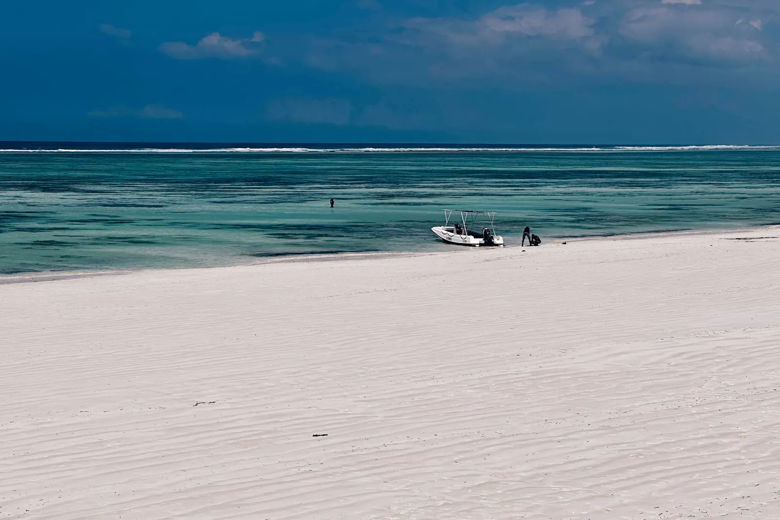 Breiter weißer Sandstrand bei Matemwe, dahinter die türkisfarbene Lagune mit einem Motorboot