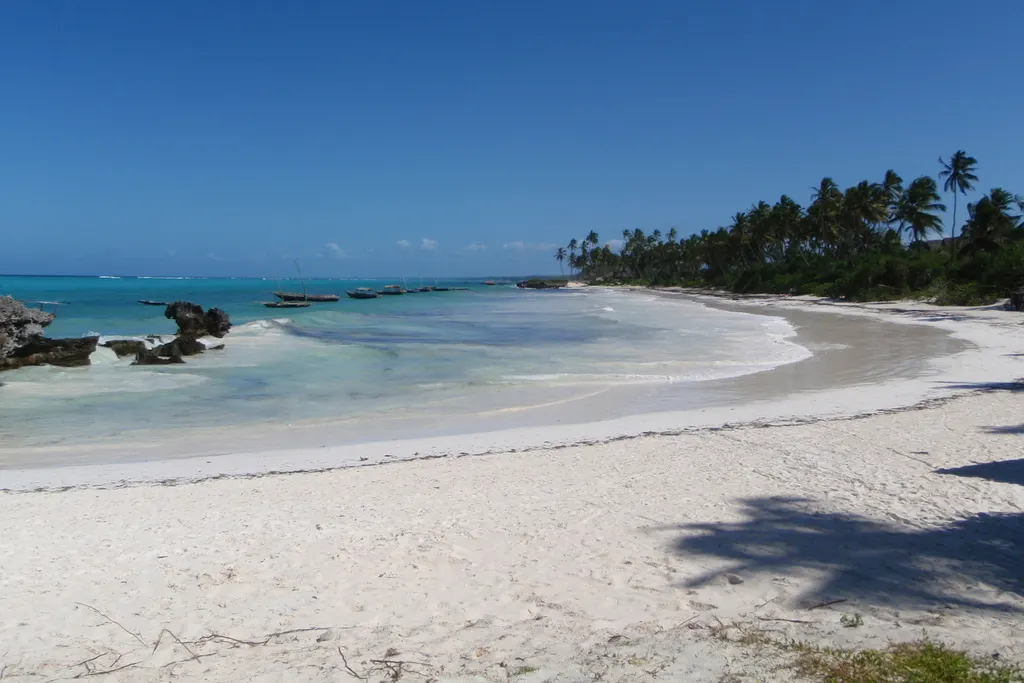 Weißer Sandstrand bei Matemwe mit Palmen, flachem türkisfarbenem Wasser und Booten in der Bucht