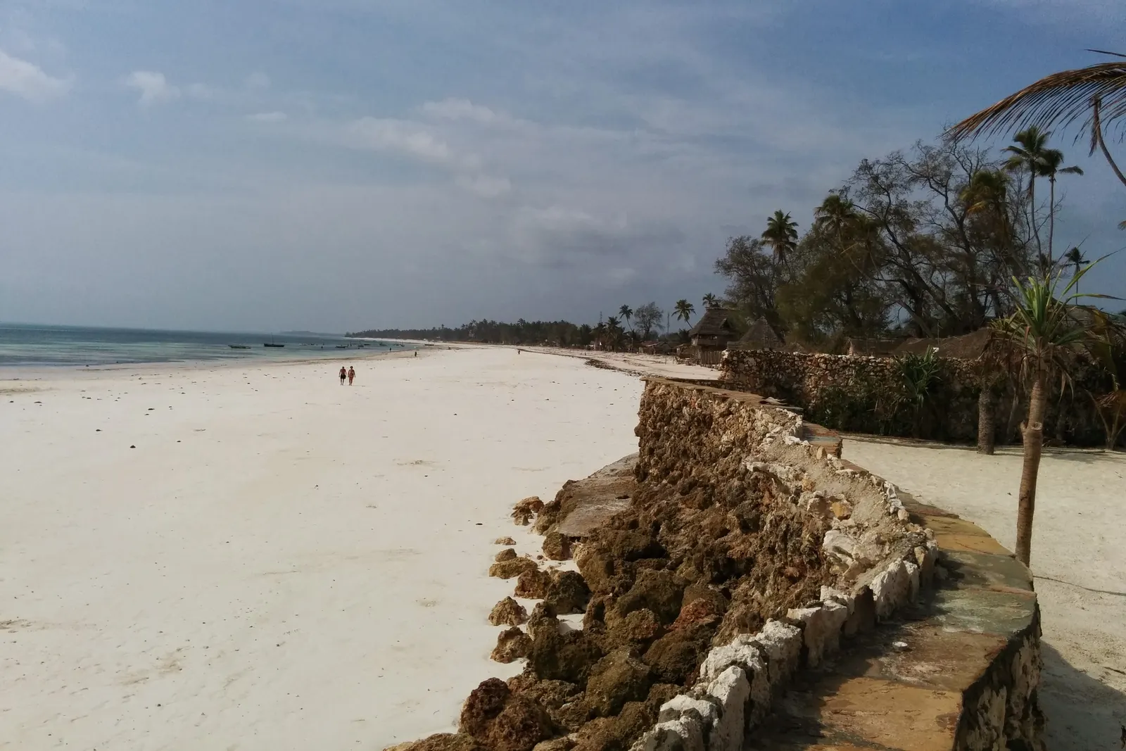 Blick von Norden über die Bucht von Uroa: Sandstrand, Steinmauer und Bäume am Ufer