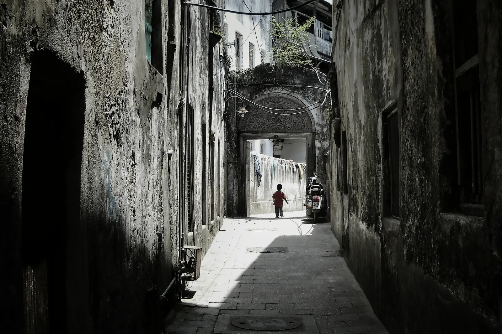 Schmale Gasse in Stone Town zwischen alten Mauern, am Ende ein Torbogen mit geschnitzter Verzierung